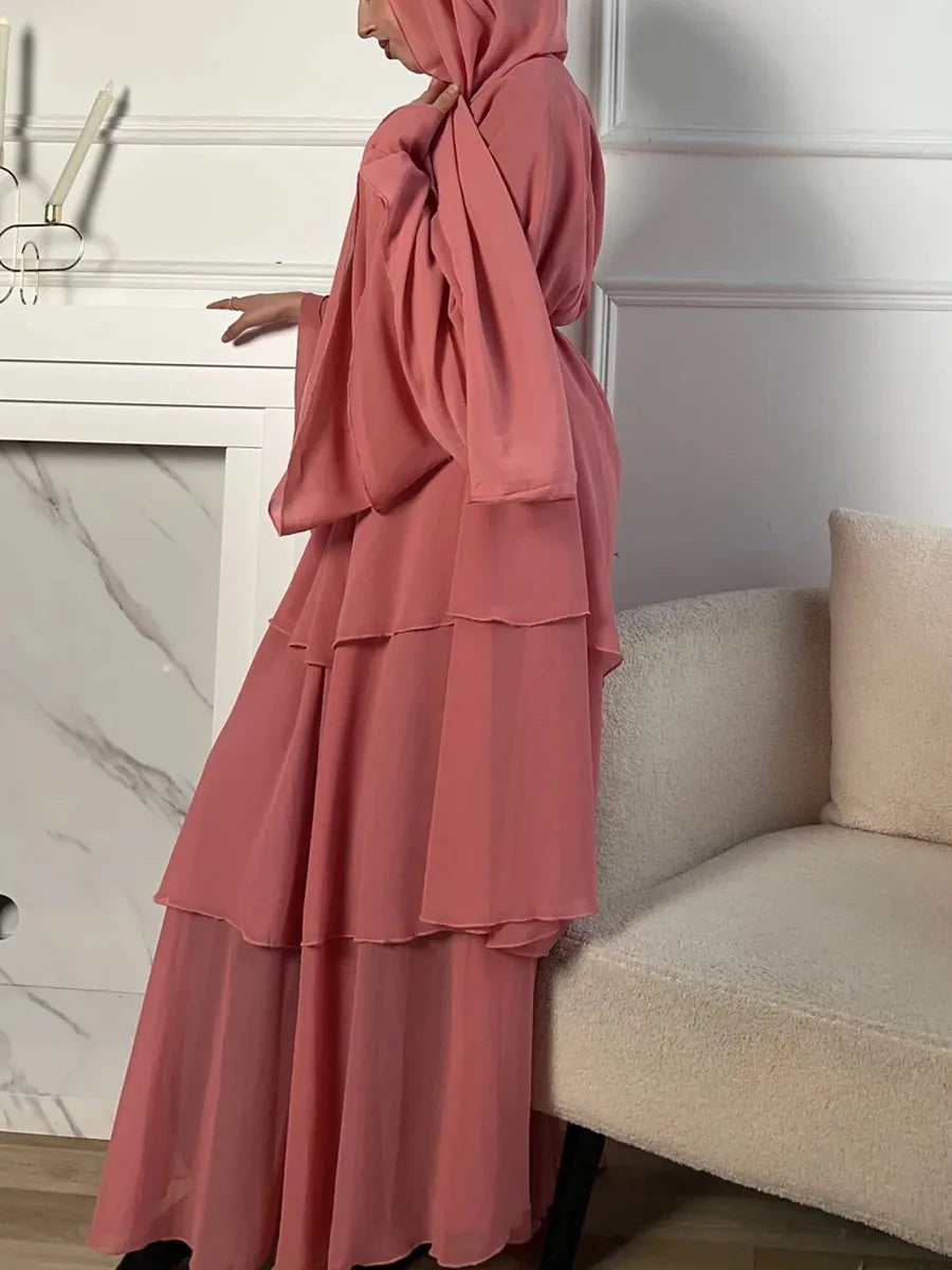 Una mujer con un elegante hijab instantáneo en color rosa, con un diseño fluido y en capas, posando en un ambiente minimalista con una chimenea y un sillón beige.